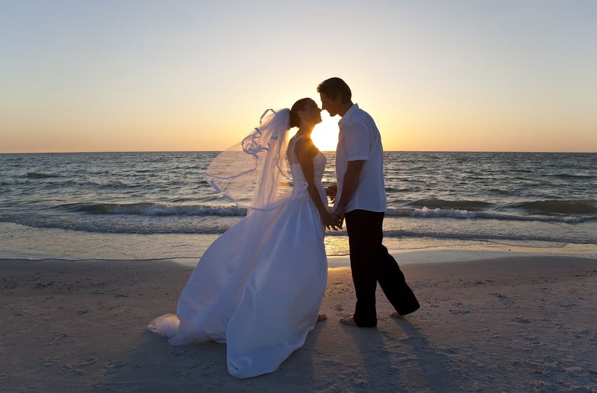 Bride and groom kissing on the beach during sunset.