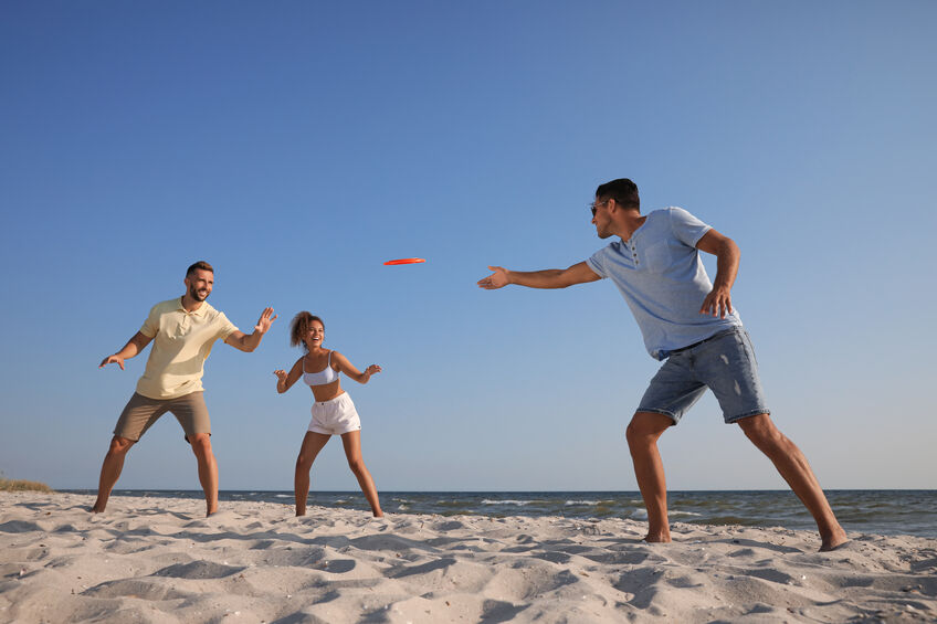 Friends playing with frisbee at beach on sunny day