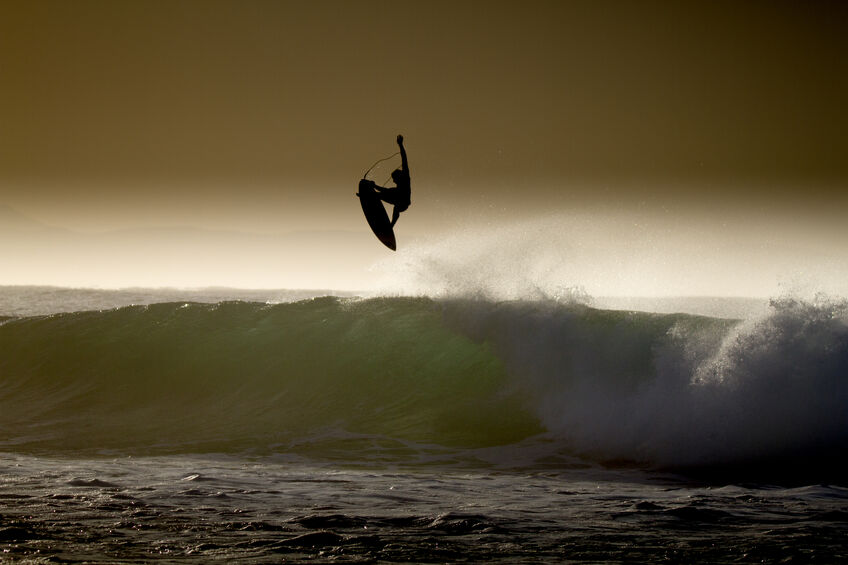 Surfer in silhouette doing aerial on wave during practice for world championship