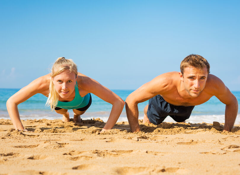 Athletic couple doing push ups on the beach, workout training